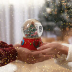 Couple,Holding,Snow,Globe,With,Christmas,Tree,At,Home,,Closeup